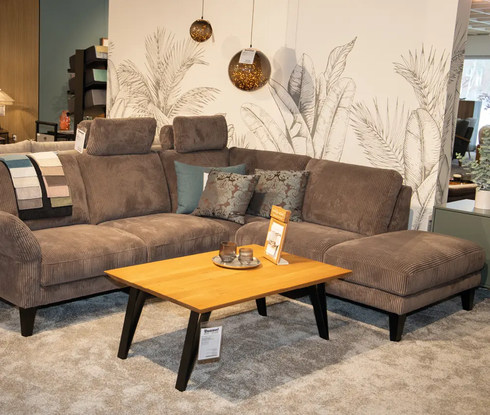 Großes Ecksofa in Braun mit Kissen und Stoffmustern, davor rechteckiger Couchtisch aus Holz auf grauem Teppich im Möbelhaus